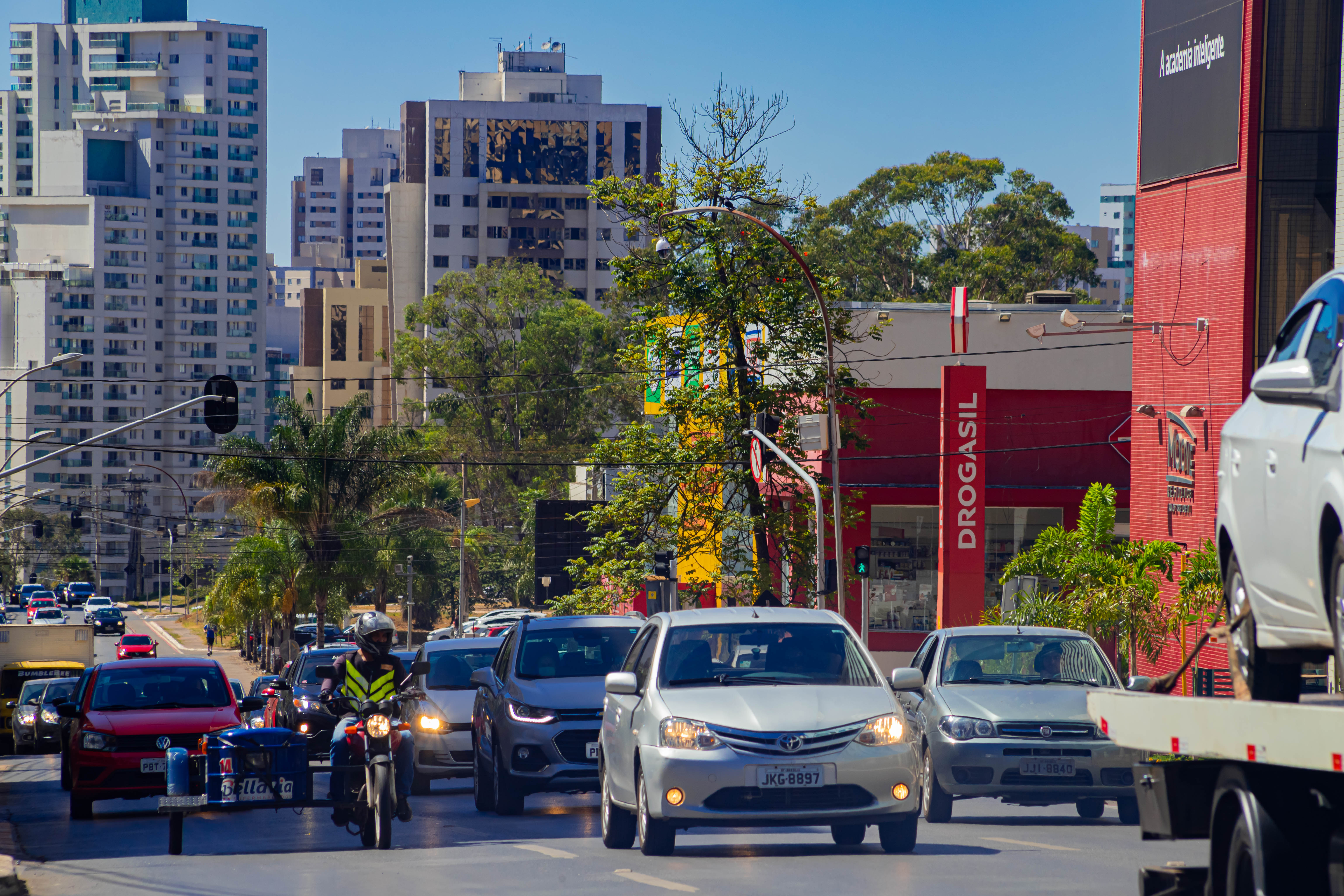 Avenida principal de Águas Claras com carros parados, prédios ao fundo e céu azul ilustrando o tempo quente.